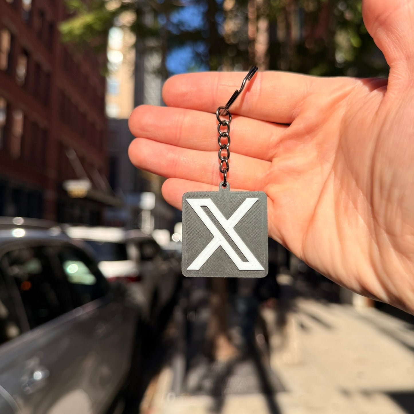 Hand holding a keychain with a 'X' symbol in an urban setting