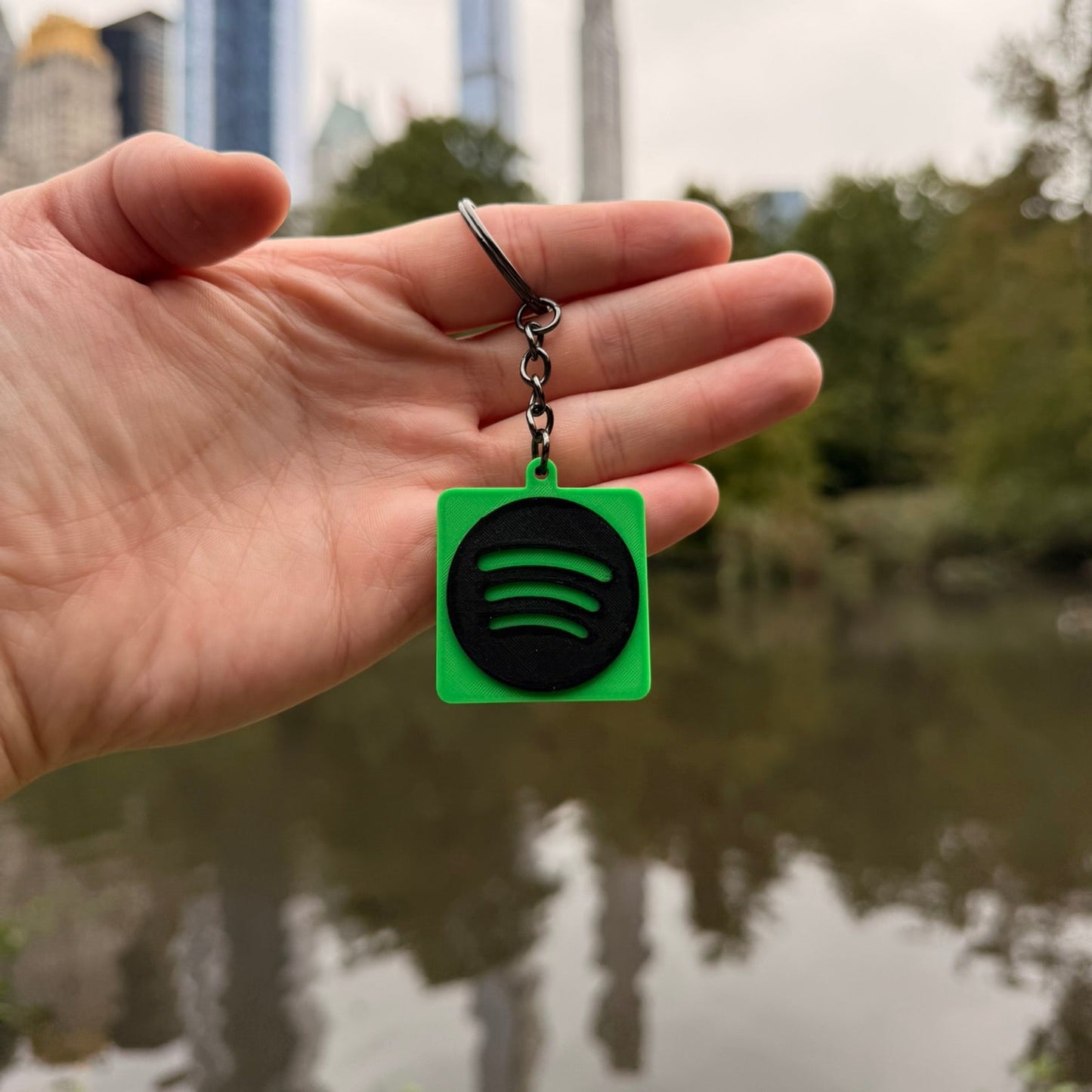 Hand holding a Spotify keychain with a cityscape in the background