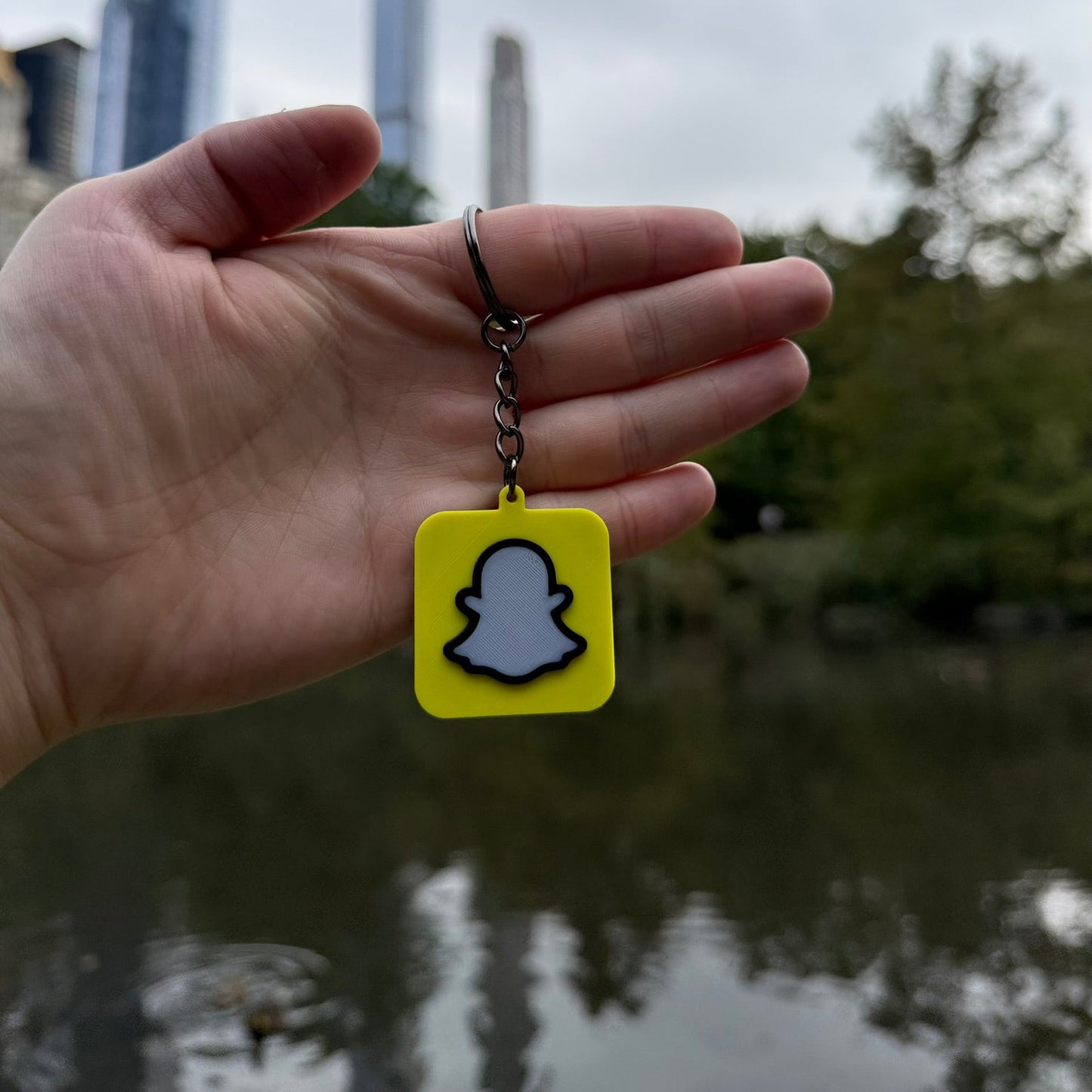 Hand holding a Snapchat keychain with a blurred cityscape in the background