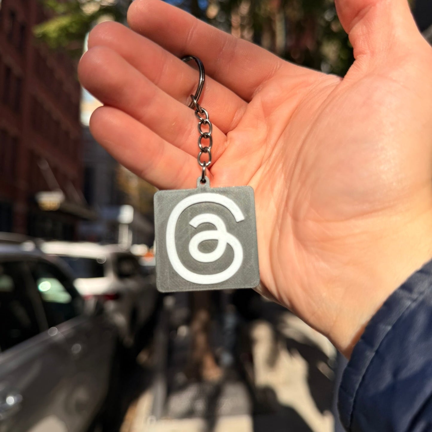 Hand holding a keychain with a logo against an urban background
