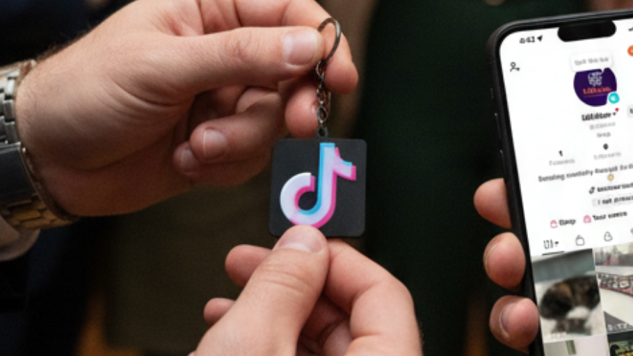 Person holding a TikTok keychain and a smartphone with TikTok app open.